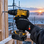 Main d'ouvrier avec gant chauffant fin PAREBISE qui visse à la perceuse sur un chantier à l'aube